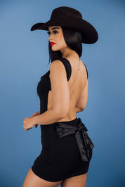Black mini dress features cap sleeves, a scoop neckline, and an open-back design accented by a large satin bow at the lower back.