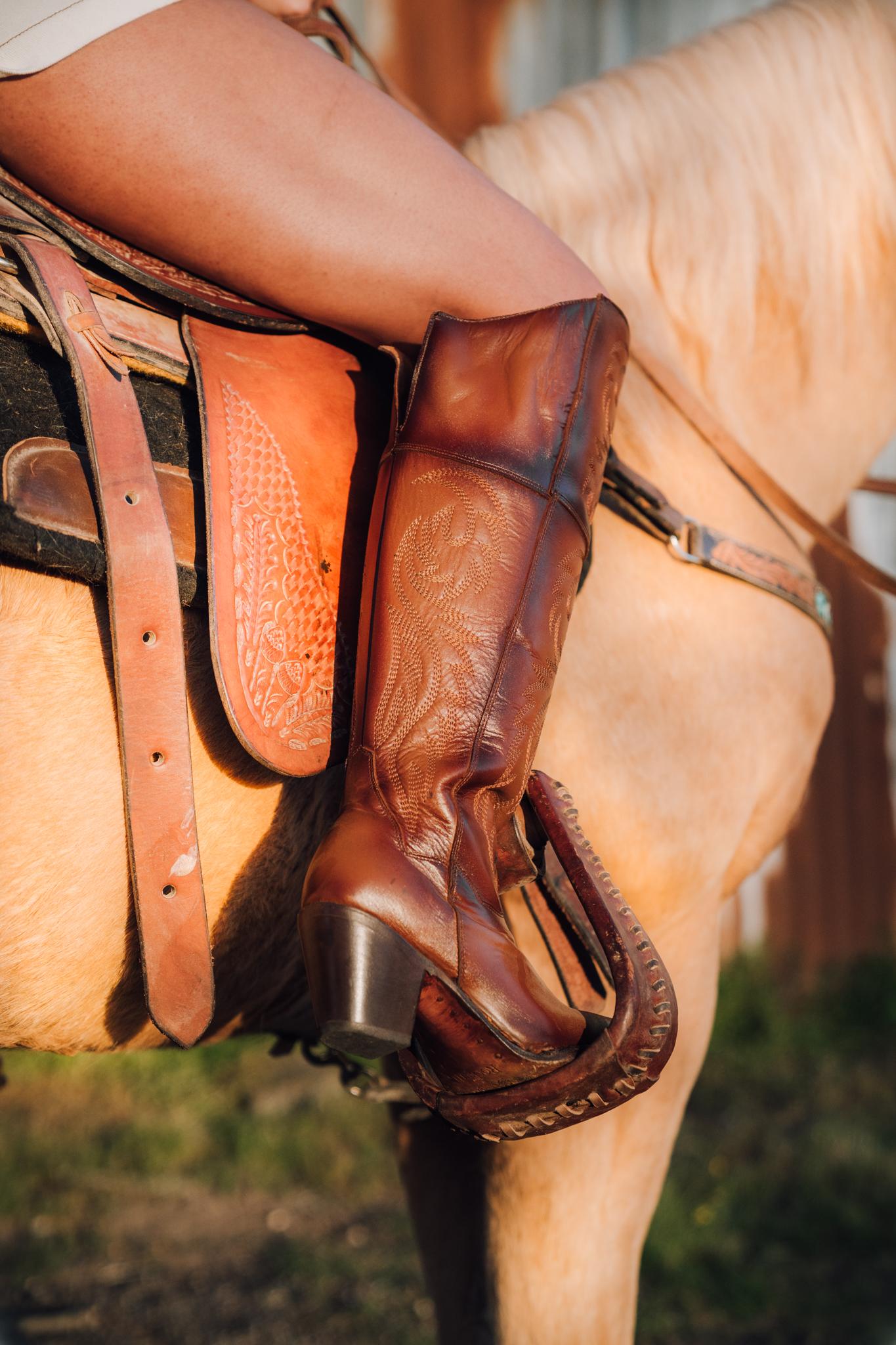Zoom in of a  woman's leg on a horse while wearing a Rock'em Brown Boot