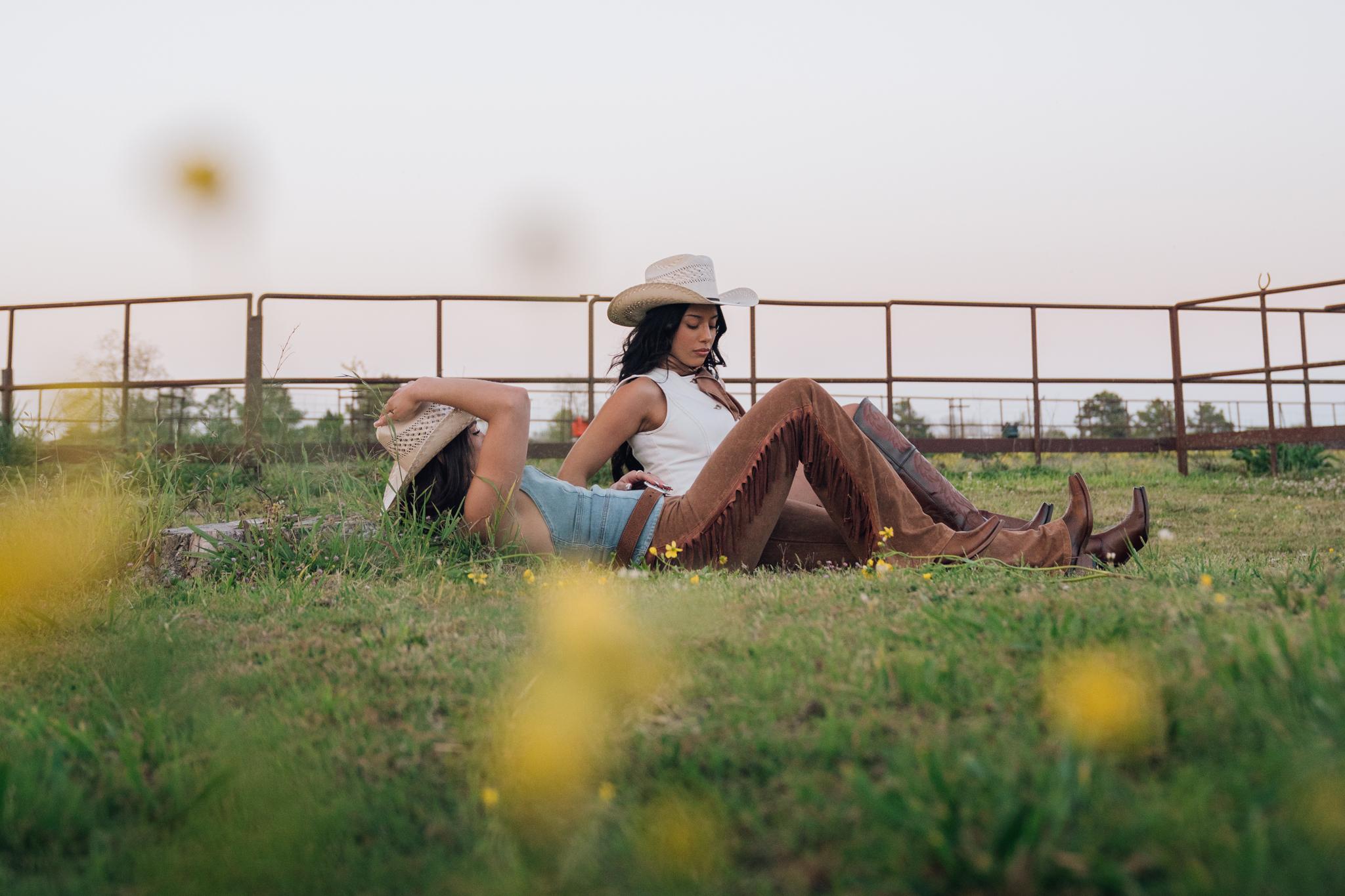 Two women laying on the grass wearing Rock'em straw hats, apparel, and boots