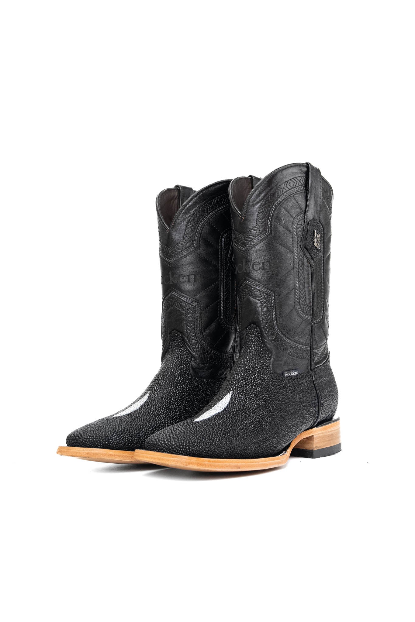 The Barnet Stingray Exotic is an all-black cowboy boot crafted from genuine leather. It showcases a square toe, an exotic stingray vamp with pebbled texture and a white diamond-shaped marking in the middle, Rock'em embroidered in the leather shaft, rubber heel, and leather sole.