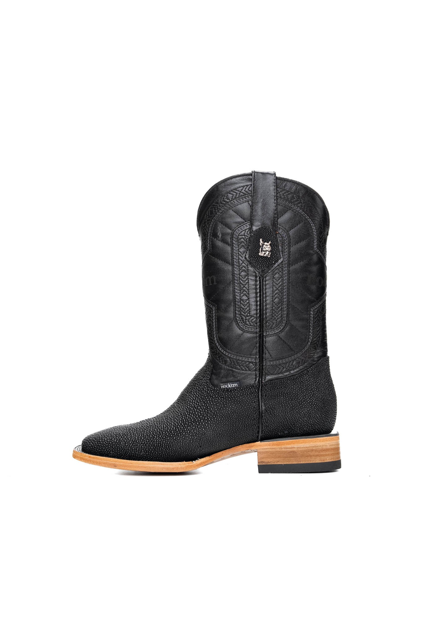 Side view of the Barnet Stingray Exotic, an all-black cowboy boot made from genuine leather. It features a square toe, a stingray vamp with a pebbled texture and a white diamond-shaped marking, an embroidered "Rock'em" logo on the leather shaft, a rubber heel, and leather sole.