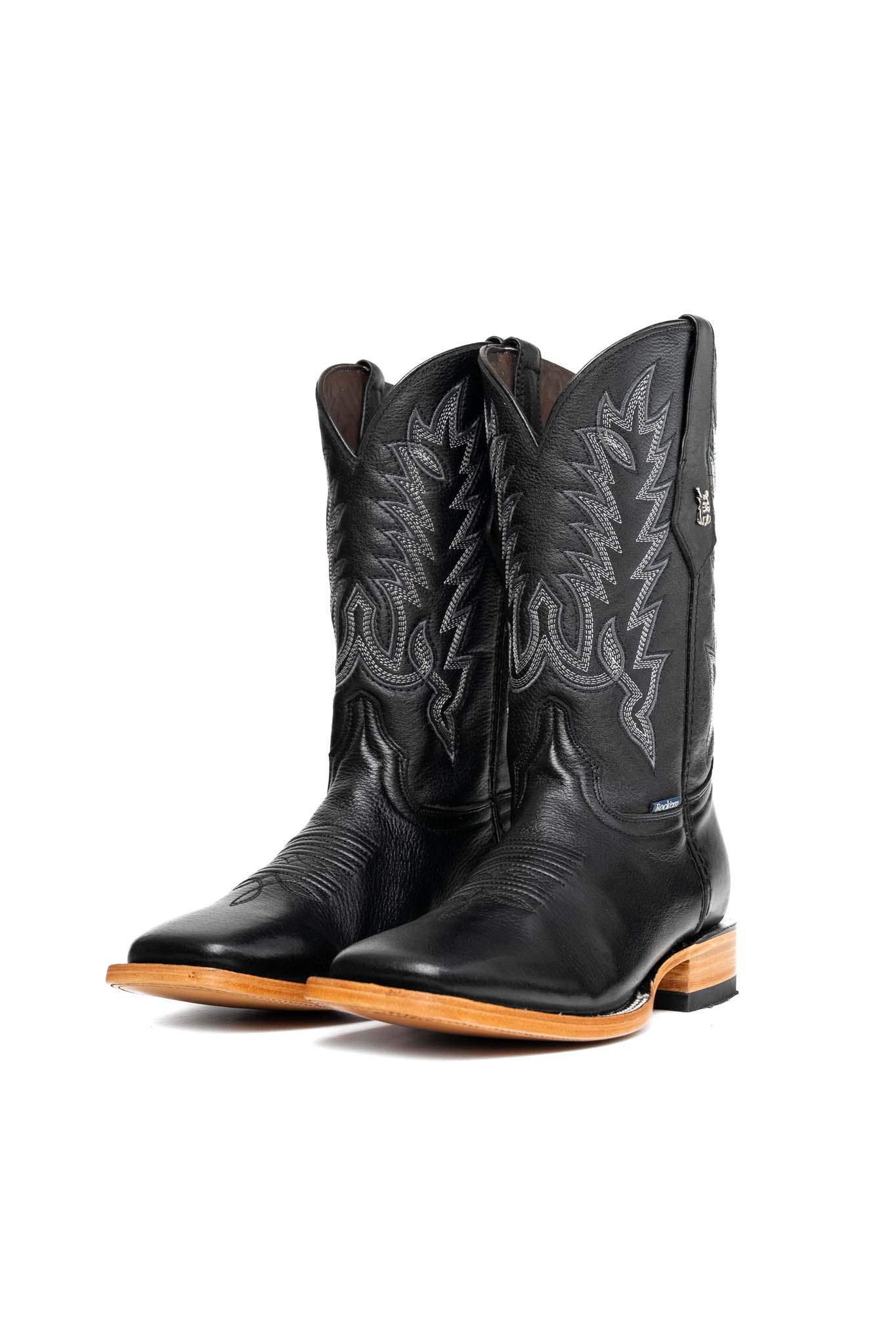 The Heritage Rainbow cowboy boots feature black leather with intricate stitching and embroidery, a Rock'em bull emblem, durable leather sole, and rubber heel.