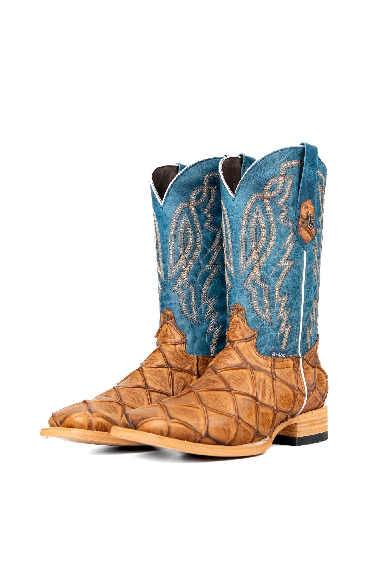The Renegate Big Bass Pirarucu boot features a tan Pirarucu fish print vamp, a blue leather shaft with embroidery, a square toe, and leather sole. 