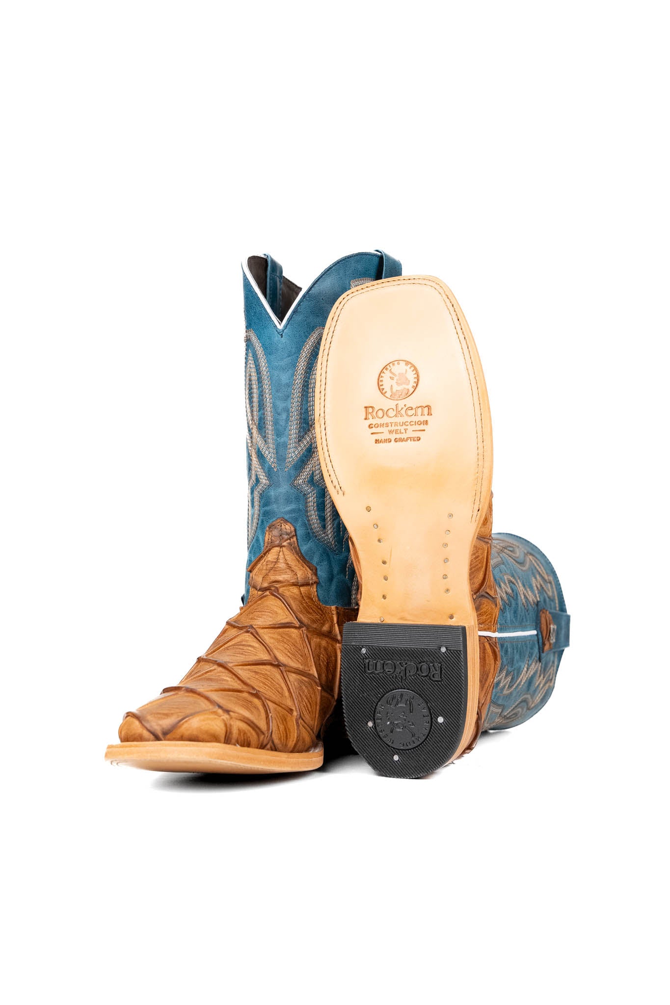 View of the Renegate Big Bass Pirarucu boot features a tan Pirarucu fish print vamp, a blue leather shaft with embroidery, a square toe, and leather sole. 