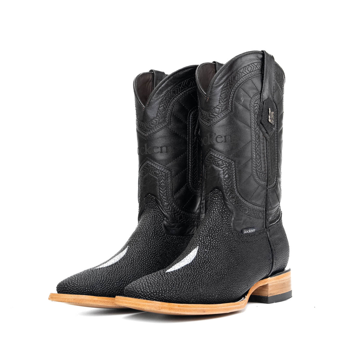 The Barnet Stingray Exotic is an all-black cowboy boot crafted from genuine leather. It showcases a square toe, an exotic stingray vamp with pebbled texture and a white diamond-shaped marking in the middle, Rock'em embroidered in the leather shaft, rubber heel, and leather sole.
