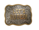 Close up shot of a silver gold belt buckle that says "Lets's rodeo!" in the middle.