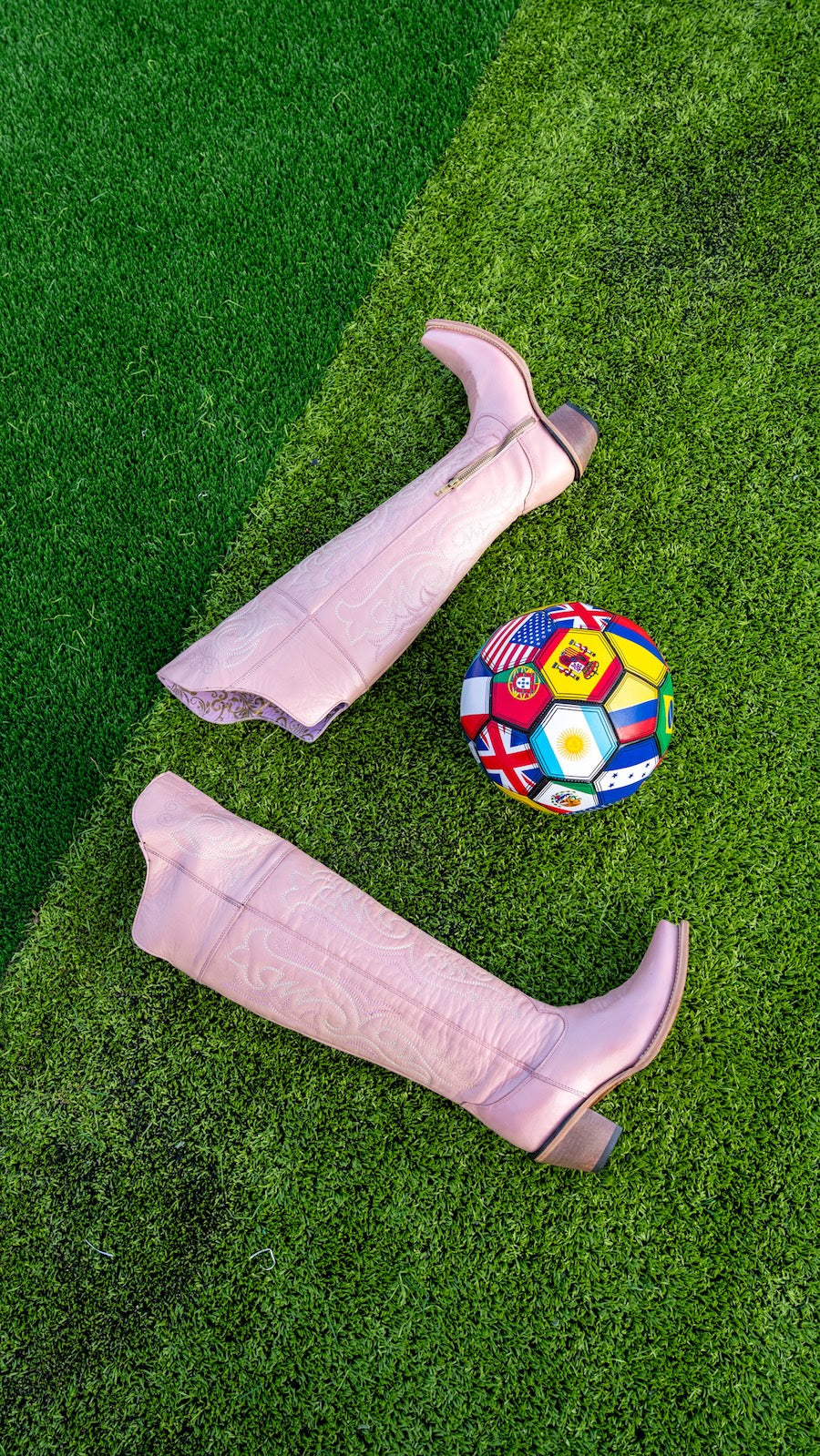 Pink knee-high boots and a multicolored soccer ball on green grass