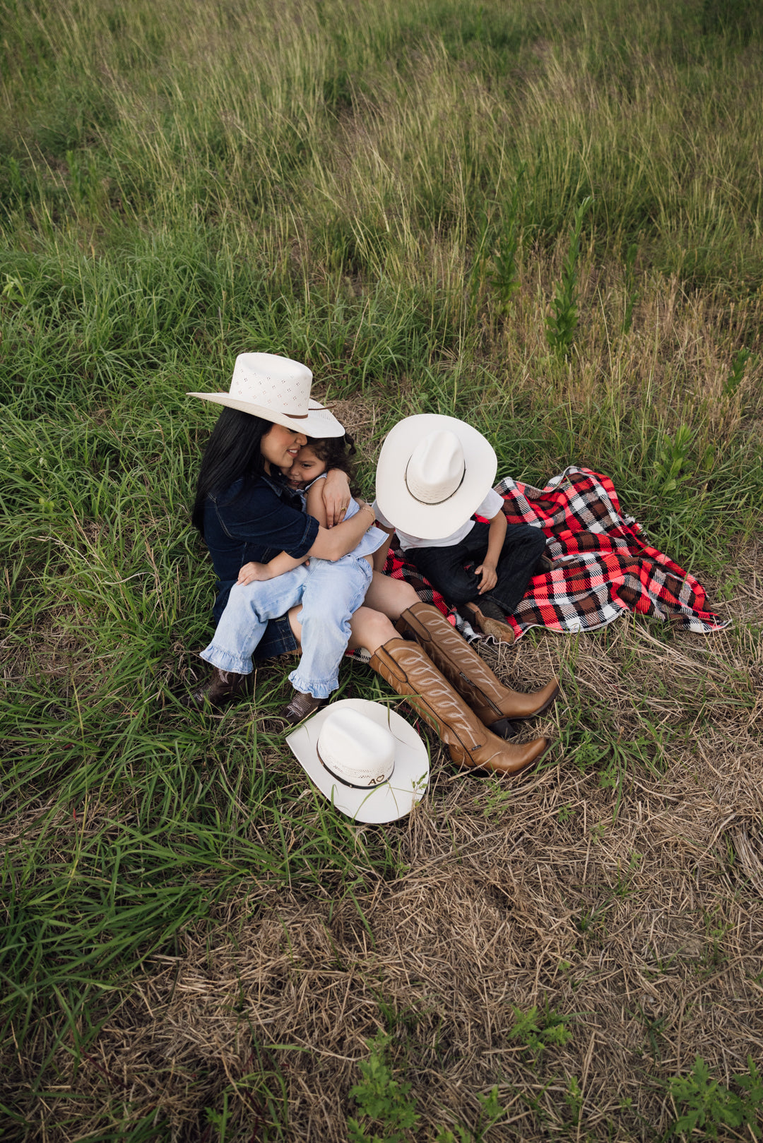 Woman wearing Rock'em boots and hat with her children laying on a field